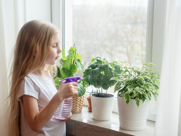 Petite fille, arrosage des plantes d'intérieur dans sa maison