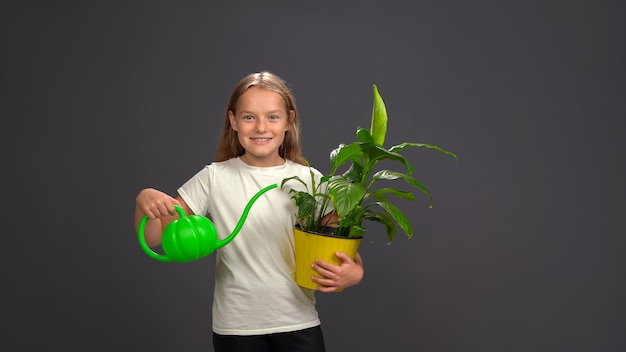 Petite fille arrosant une fleur dans un pot à l'aide d'un drôle d'arrosoir tenant tout dans ses mains