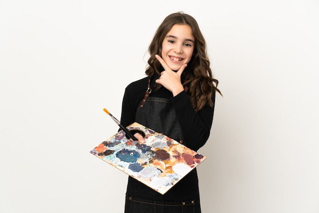 Petite fille artiste tenant une palette isolée sur un mur blanc heureux et souriant