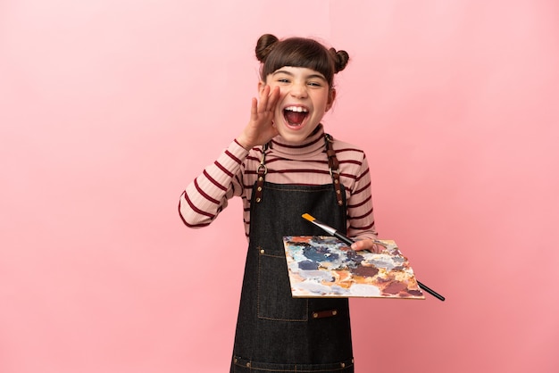 Petite fille artiste tenant une palette isolée sur un mur rose en criant avec la bouche grande ouverte