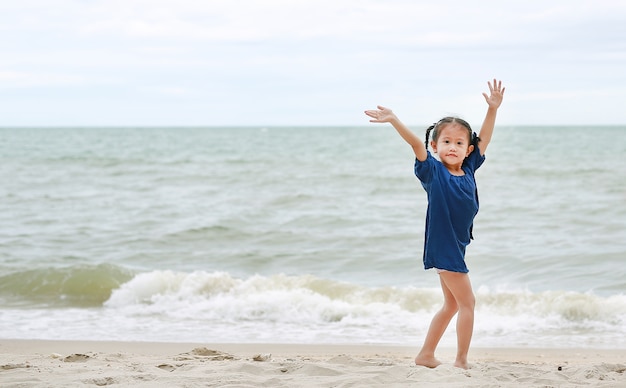 Petite fille asiatique agitant sa main en disant au revoir sur la plage