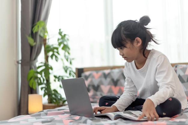 Petite fille asiatique à l'aide d'un ordinateur portable en position allongée sur le lit