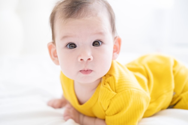 Une petite fille asiatique en bonne santé de 5 mois en body jaune sur le lit sur une literie blanche