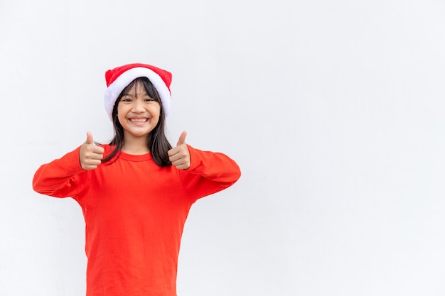 Petite fille asiatique en bonnet de Noel rouge sur fond blanc.