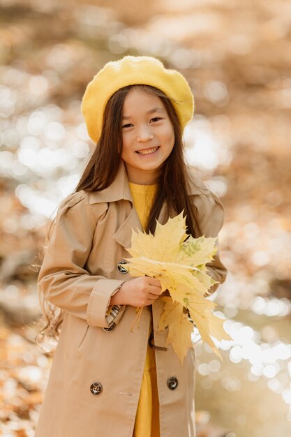 Une petite fille asiatique brune en vêtements d'automne se promène dans la forêt d'automne près d'un ruisseau