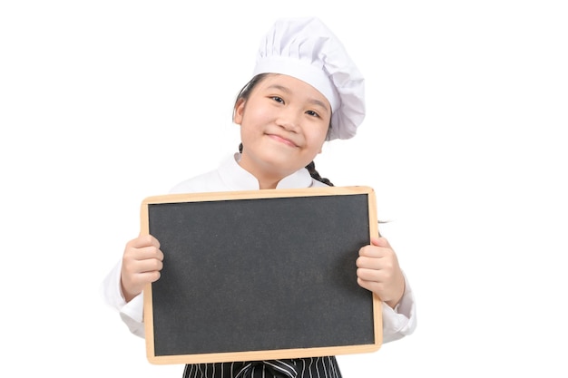 Petite fille asiatique chef cuisinier en uniforme tenant un tableau noir pour mettre du texte ou un menu, isolé sur fond blanc