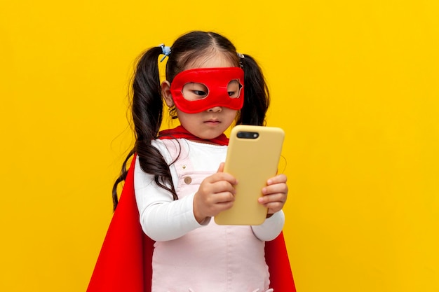 petite fille asiatique en costume et masque de superman utilise un smartphone coréen enfant en cape de super-héros