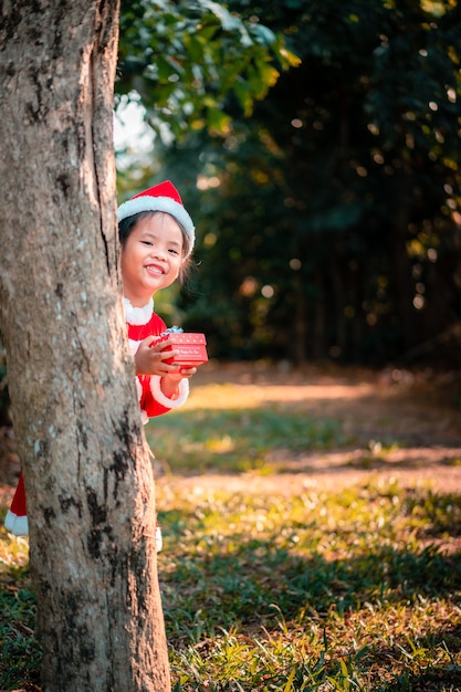 Petite fille asiatique en costume de père Noël rouge avec présent fort dans le parc