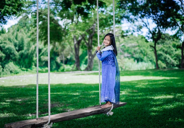 Petite fille asiatique en costume de princesse jouant une balançoire en bois dans le parc