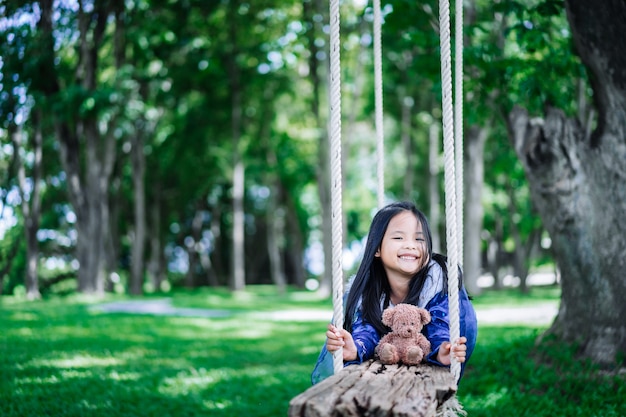 Petite fille asiatique en costume de princesse jouant à l'ours sur une balançoire en bois dans le parc