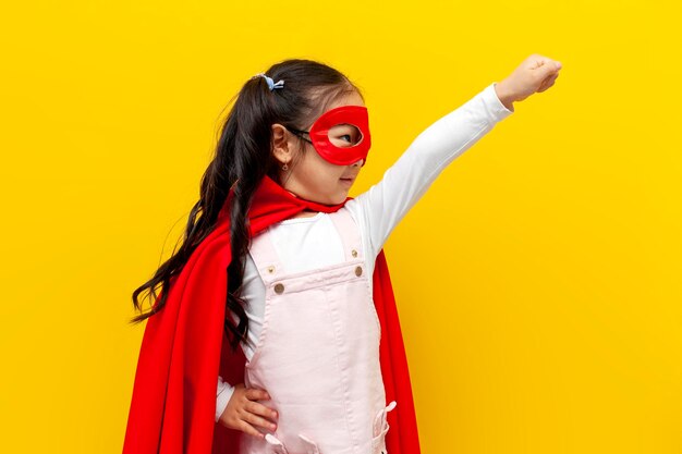 Petite fille asiatique en costume de superman et masque montre avec sa main en avant et vole