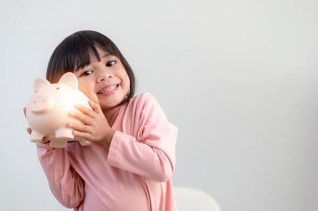 Petite fille asiatique économisant de l'argent dans une tirelire, apprenant à économiser, Kid économiser de l'argent pour l'éducation future. Concept d'argent, de finances, d'assurance et de personnes