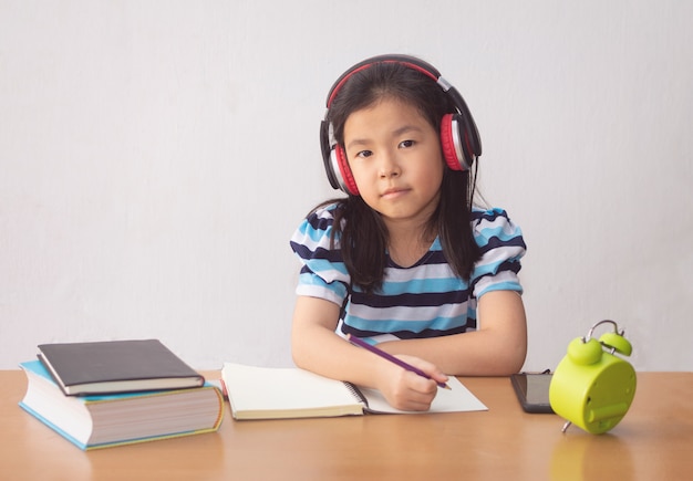 Petite fille asiatique écrivant un livre et un casque d'écoute de la musique.