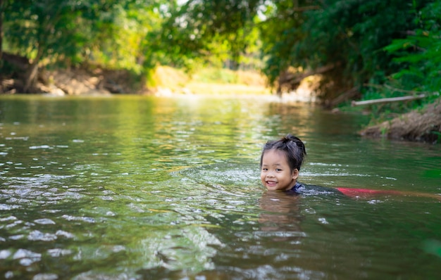 Petite fille asiatique jouant dans la rivière avec la lumière du soleil