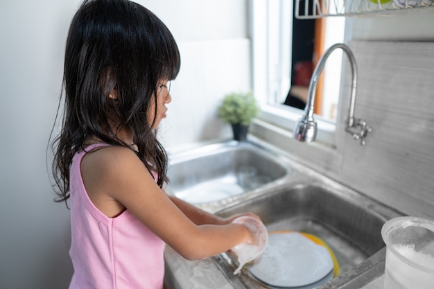 Petite fille asiatique lave la vaisselle dans la cuisine