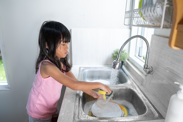 Petite fille asiatique lave la vaisselle dans la cuisine