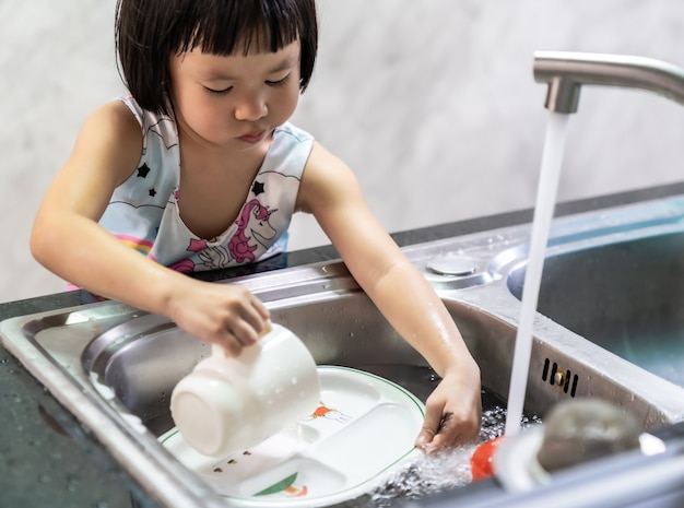 Petite fille asiatique lave la vaisselle