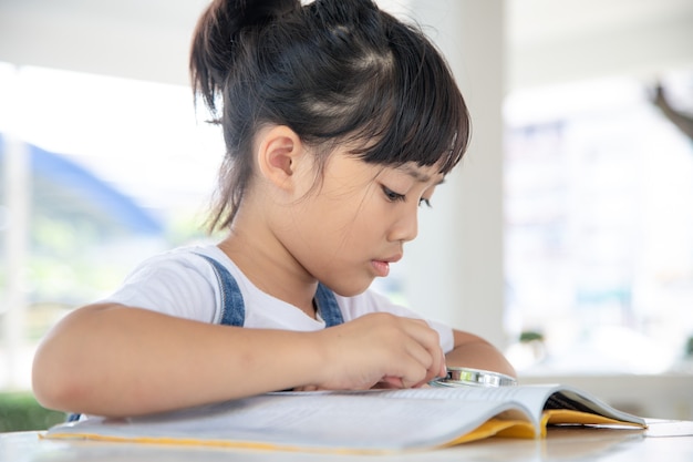 Petite fille asiatique lisant les livres sur le bureau avec une loupe