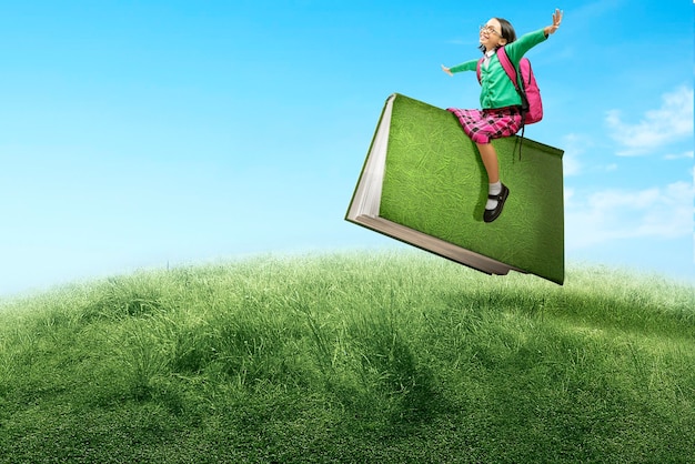 Petite fille asiatique avec des lunettes assise sur un livre volant Journée mondiale du livre