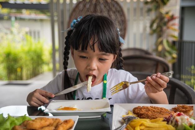 Petite fille asiatique mange un œuf au plat sur un plat à table