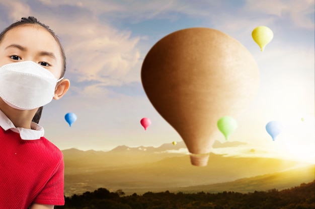 Petite fille asiatique avec masque facial avec ballon à air coloré volant avec fond de ciel coucher de soleil