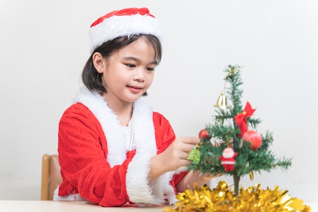 Une petite fille asiatique mignonne dans une robe rouge de père Noël décorant l'arbre de Noël la veille de Noël