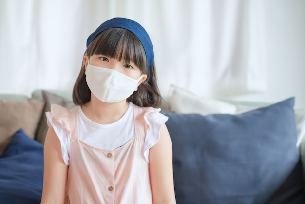 Une petite fille asiatique mignonne portant un masque hygiénique pour prévenir le coronavirus ou l'épidémie de Covid-19 maintient la distance sociale et reste à la maison.