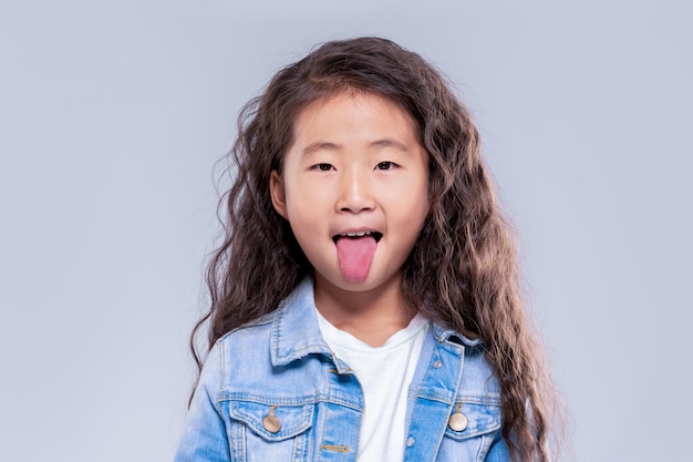 Une petite fille asiatique montre sa langue à la caméra Ambiance ludique Sur le fond du net dans le studio