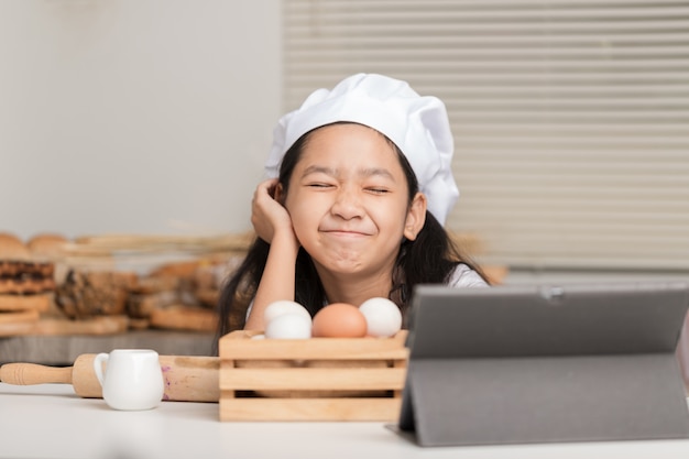 Une petite fille asiatique portant un chapeau de chef blanc et souriant joyeusement avec le premier plan flou.