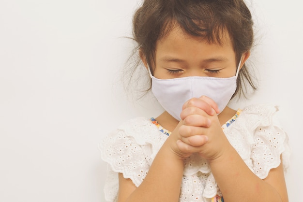 Petite fille asiatique portant un masque et priant. Mains jointes dans le concept de prière, espace de copie.