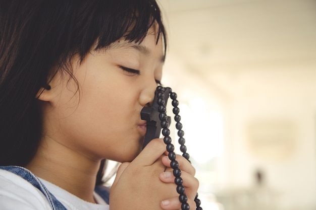 Petite fille asiatique priant en tenant la croix, concept chrétien.