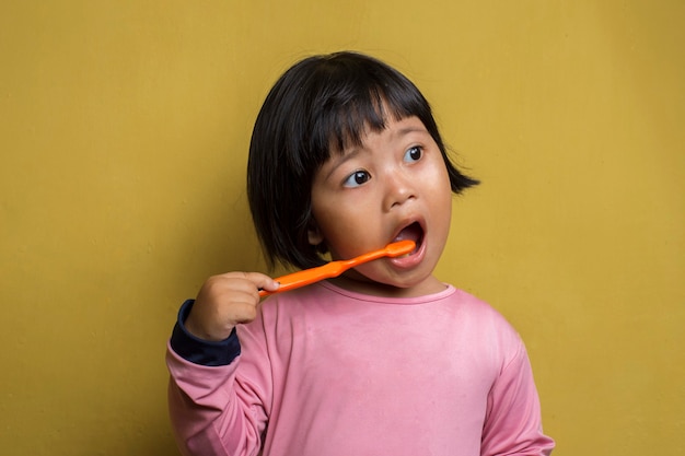 Petite fille asiatique se brosser les dents sur le mur jaune