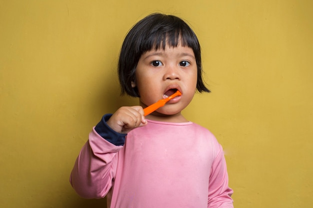 Petite fille asiatique se brosser les dents sur le mur jaune