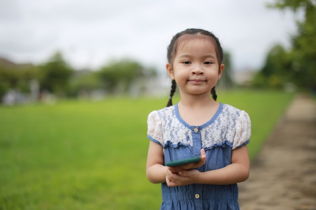 Petite fille asiatique avec un smartphone en plein air.