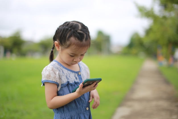 Petite fille asiatique avec un smartphone en plein air.