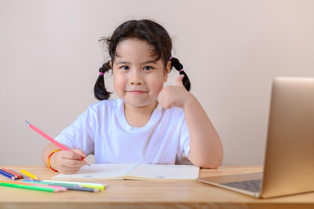 Une petite fille asiatique souriante a une classe distante d'appel vidéo avec un enseignant utilisant un ordinateur portable, une distance sociale pendant l'isolement de quarantaine pendant les soins de santé du coronavirus (COVID-19)