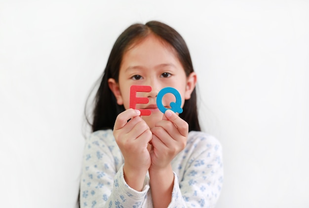 Petite fille asiatique tenant un texte éponge EQ (quotient émotionnel) sur fond blanc. Concept de développement des enfants et de l'éducation. Focus à eq texte dans ses mains