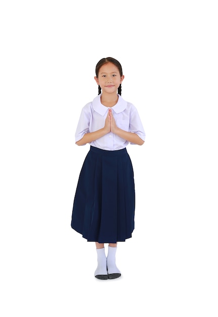 Petite fille asiatique en uniforme scolaire thaïlandais priant et debout isolé sur fond blanc. Image pleine longueur avec chemin de détourage