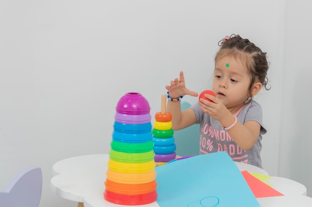 Petite fille assemblant un jouet didactique assis à une table dans une école maternelle avec espace de copie