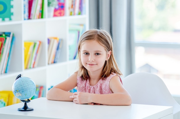 Petite fille assise au bureau dans une salle de classe légère