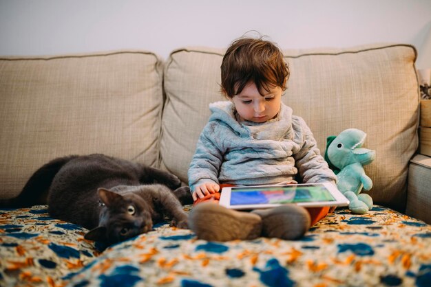 Petite fille assise sur un canapé en regardant des vidéos sur une tablette avec un chat