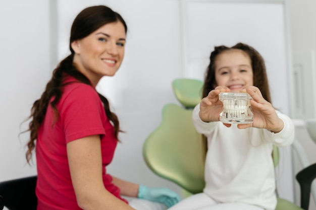 Petite fille assise sur une chaise au bureau du dentiste avec un médecin heureux à proximité