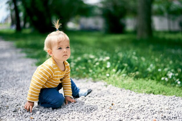 Petite fille assise sur un chemin de gravier dans un parc verdoyant