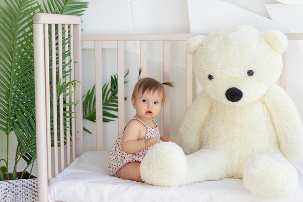 Petite fille assise dans une pièce lumineuse dans un berceau à la maison avec un gros ours en peluche