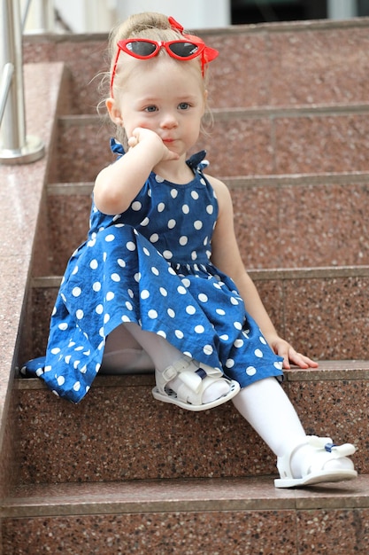 Petite fille assise dans une robe bleue sur les marches. style pin up