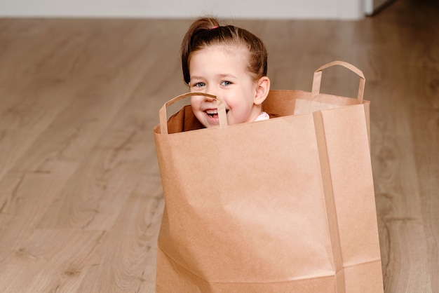 Petite fille assise dans un sac en papier brun, jouant le concept des enfants avec copie espace