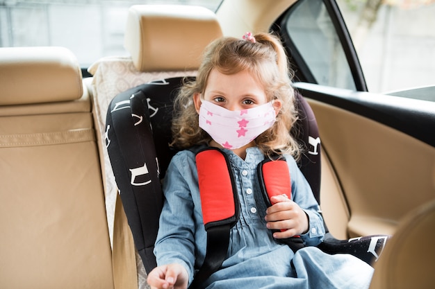 Petite fille assise dans une voiture dans un masque médical. Covid-19 Coronavirus Pandemic propagation mondiale Concept.