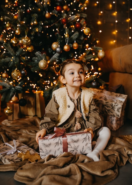 Petite fille assise devant un arbre de Noël avec des cadeaux