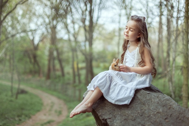 Petite fille assise sur une falaise Elle ferma les yeux et tenait un petit lapin dans ses mains