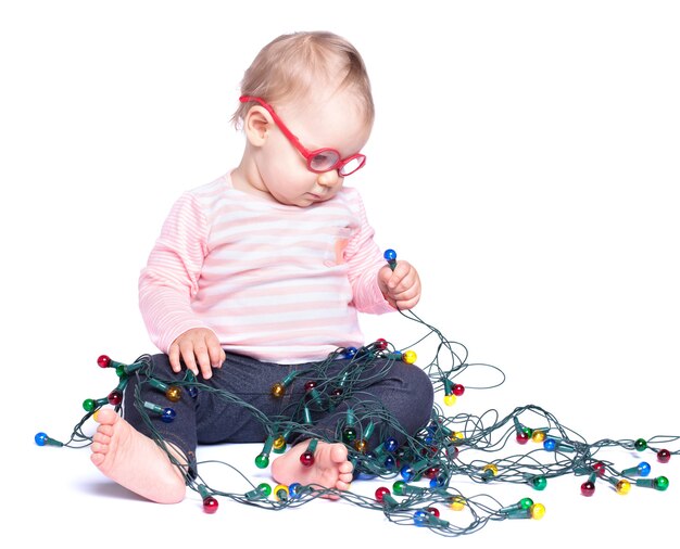 Petite fille assise sur fond blanc et jouant avec les lumières de Noël. Isolé sur blanc